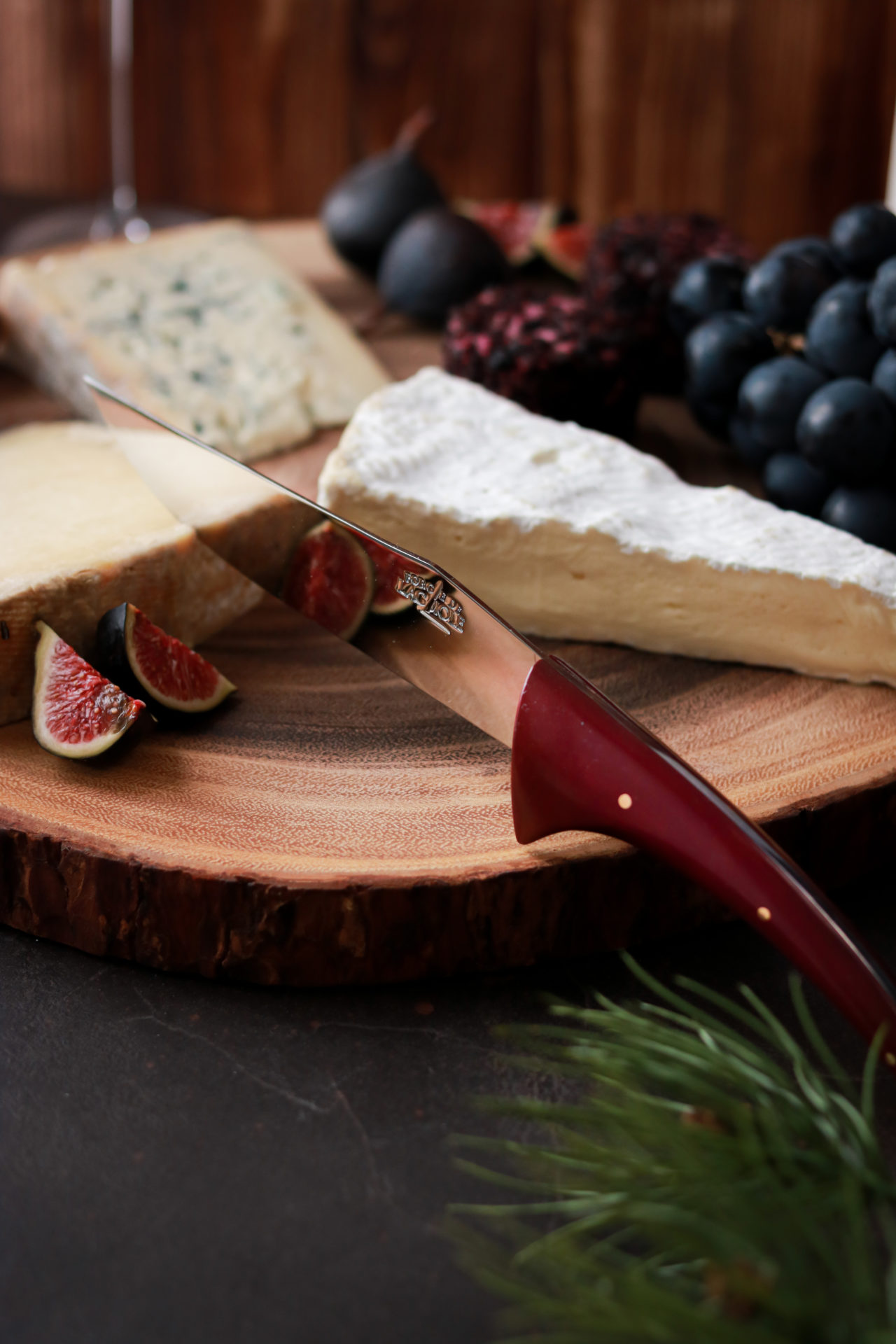 Edle Käseplatte mit Brie, Blauschimmelkäse, Hartkäse, Feigen, Trauben und einem Messer auf einem rustikalen Holzbrett