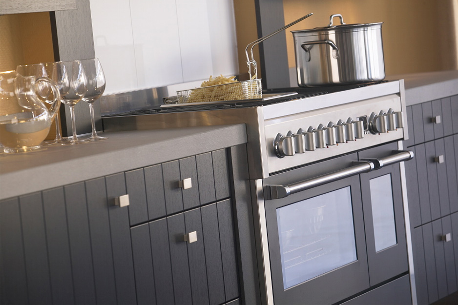 Herd mit Edelstahl-Backofen, Kochtopf und Frittierkorb sowie Weingläsern auf einer eleganten Arbeitsplatte