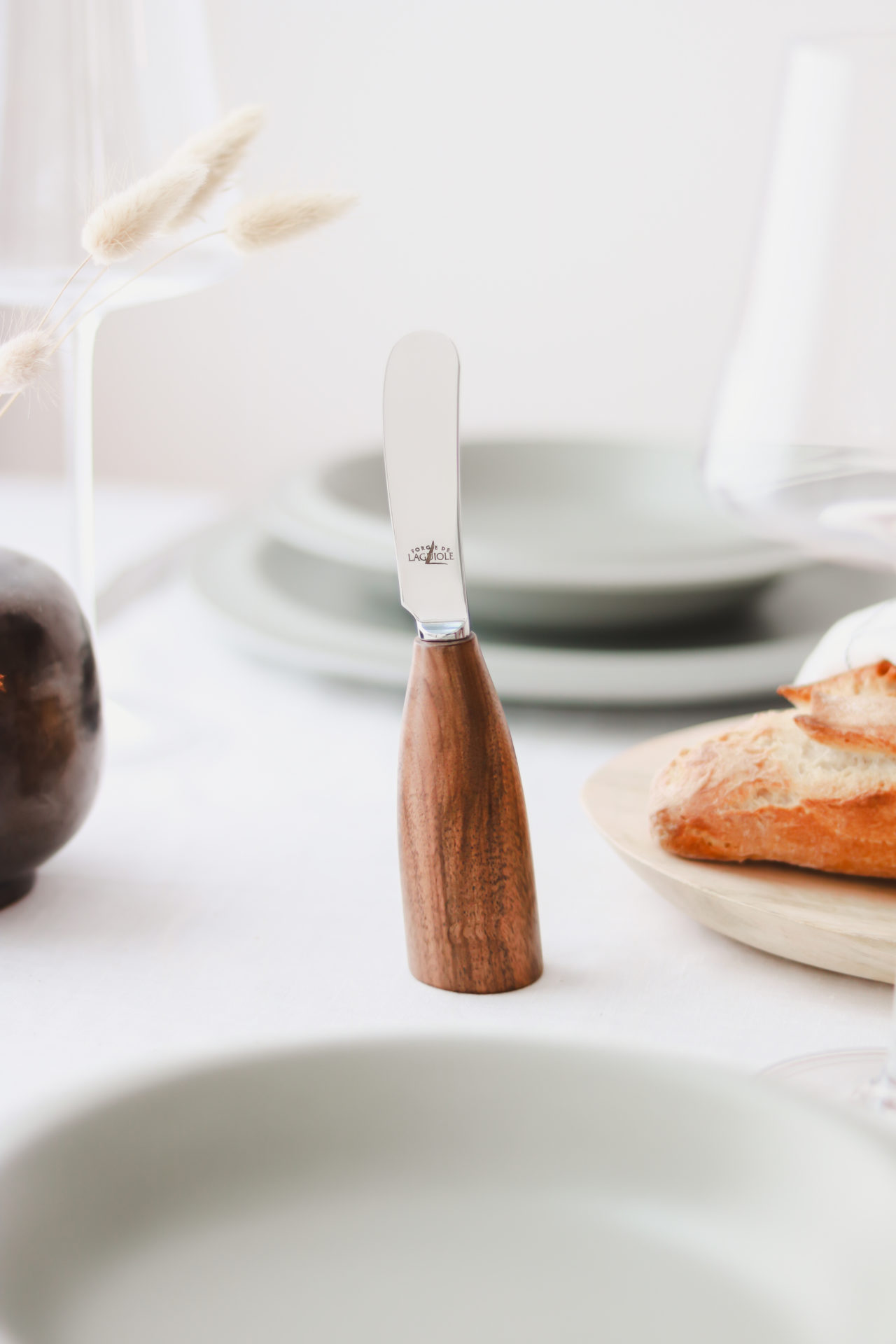 Buttermesser mit ergonomischem Holzgriff von Laguiole, stehend vor hellgrünem Geschirr und frischem Brot auf einem festlich gedeckten Tisch