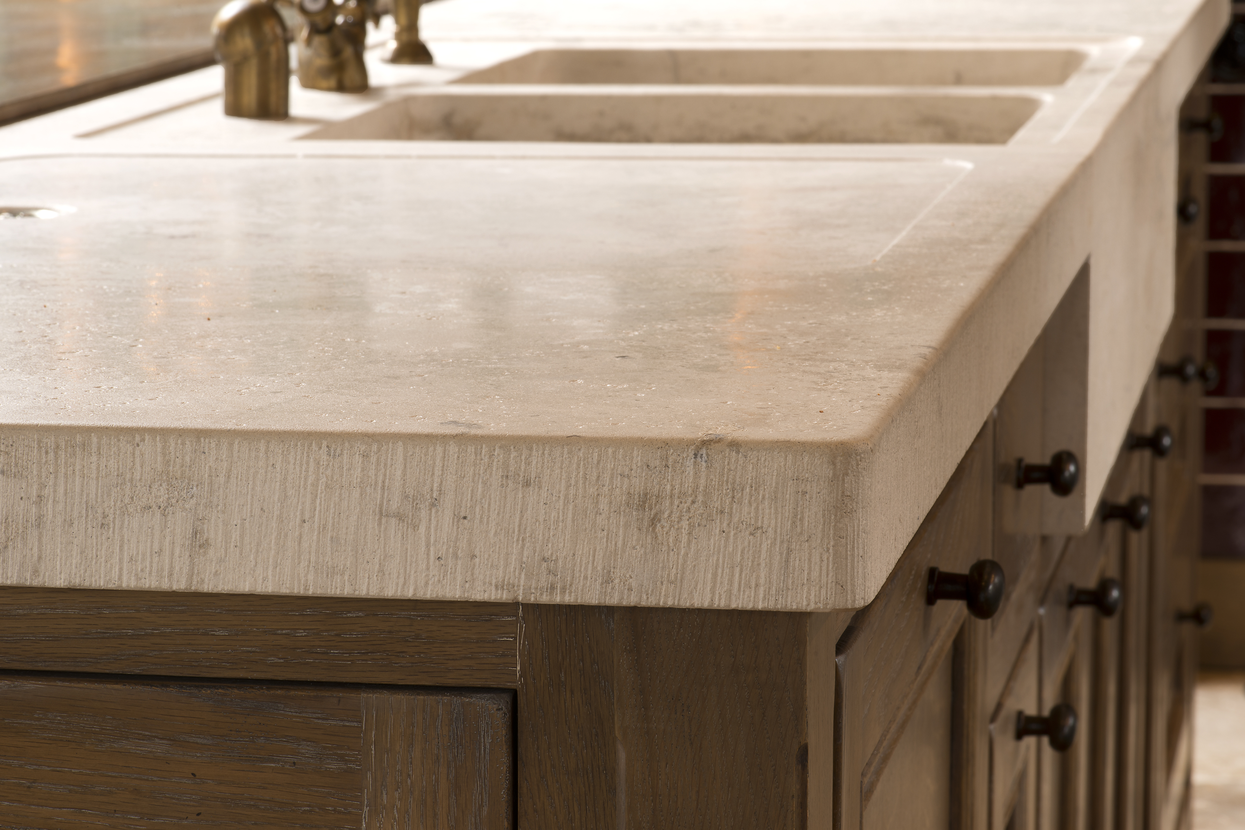 Detailansicht einer massiven Naturstein-Arbeitsplatte mit zwei Spülbecken und Holzmöbeln in einer modernen Küche