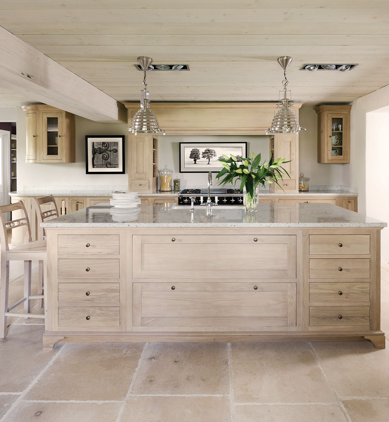 Helle Einbauküche im Landhausstil mit großer Kücheninsel, Granit-Arbeitsfläche, Holzschränken, Barhockern und eleganter Beleuchtung