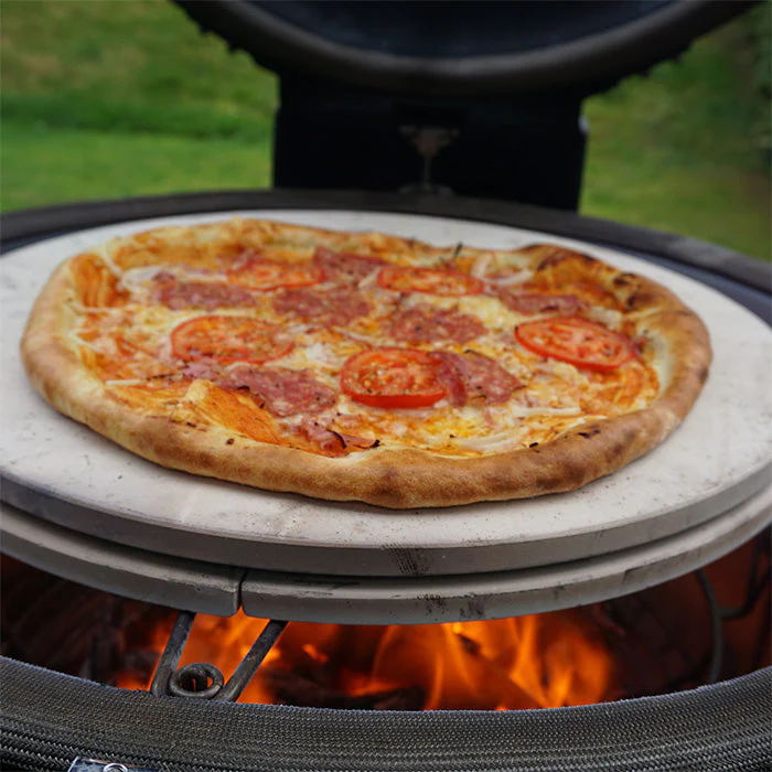 Hausgemachte Pizza mit Tomaten und Salami auf einem Pizzastein im Grill über Holzfeuer gebacken