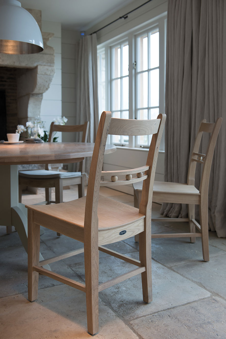 Moderner Essbereich mit hellen Holzstühlen und rundem Tisch, bodentiefe Fenster und eleganten Vorhängen