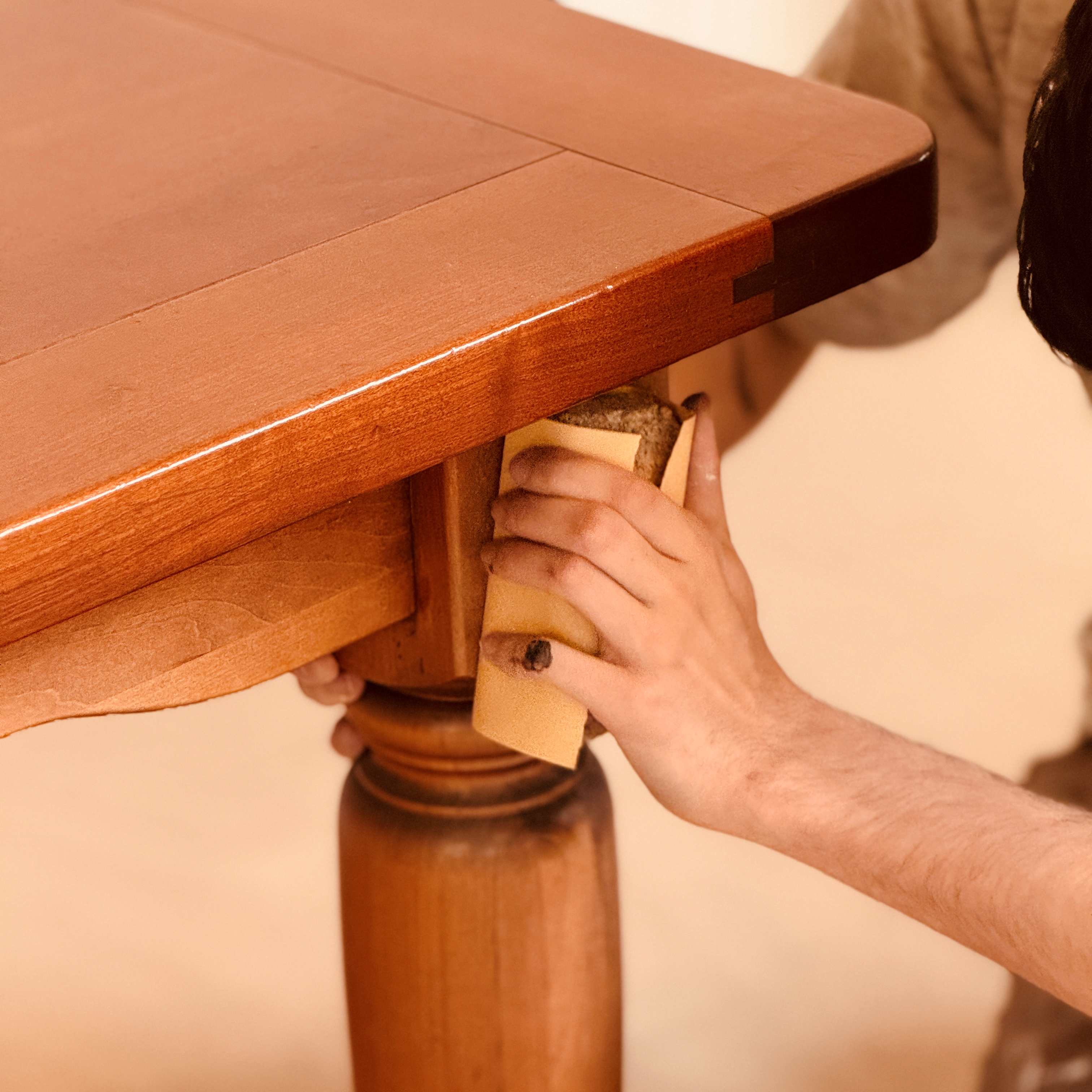 Hand trägt Holzpflege-Öl mit Schwamm auf Massivholz-Esstisch und Tischbein auf, zur Pflege, Auffrischung und Schutz der Oberfläche