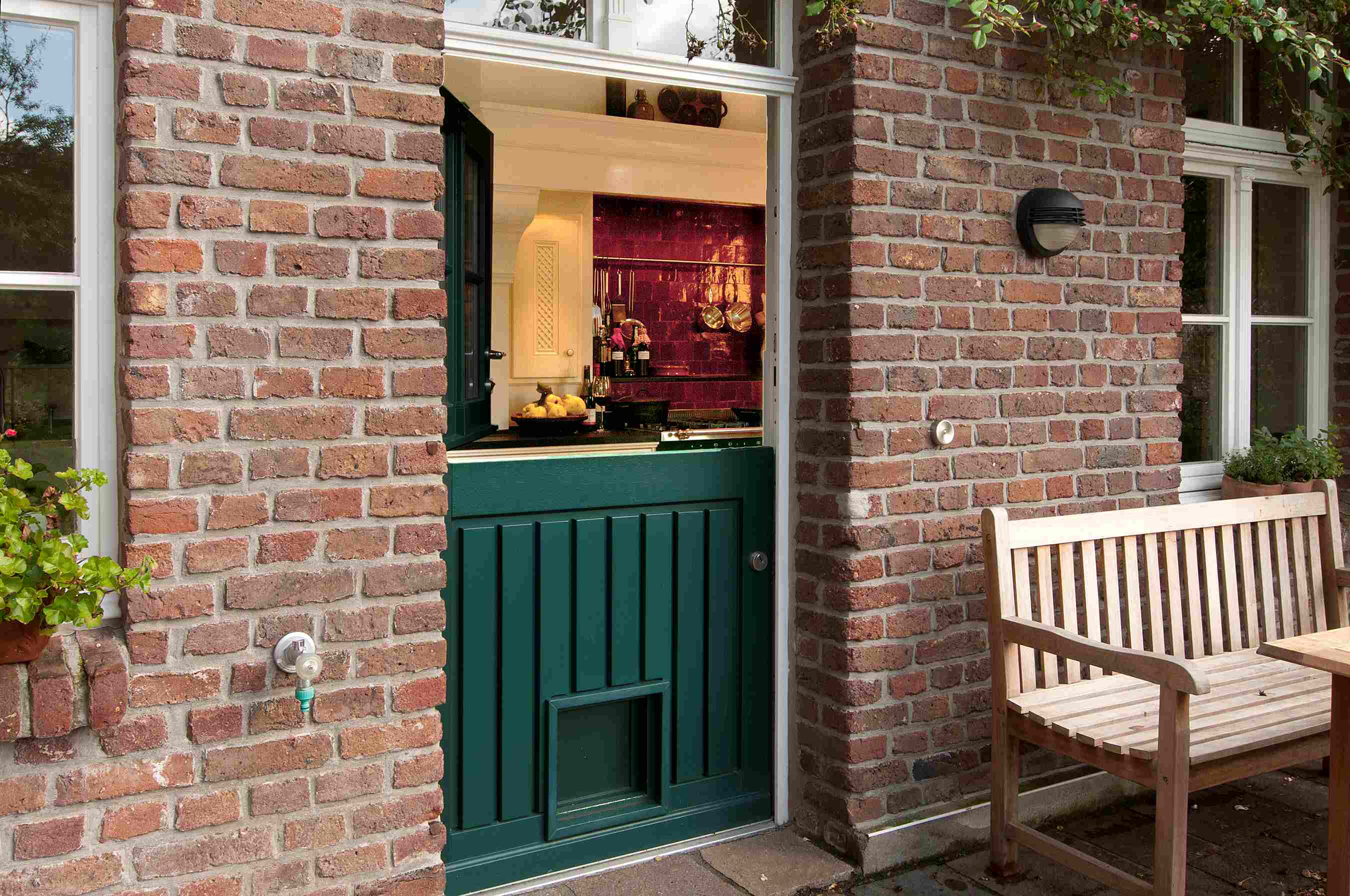 Holländische Tür in grün in einer Backsteinwand, geöffnet mit Blick in eine stilvolle Küche mit lila Kacheln und rustikalem Interieur