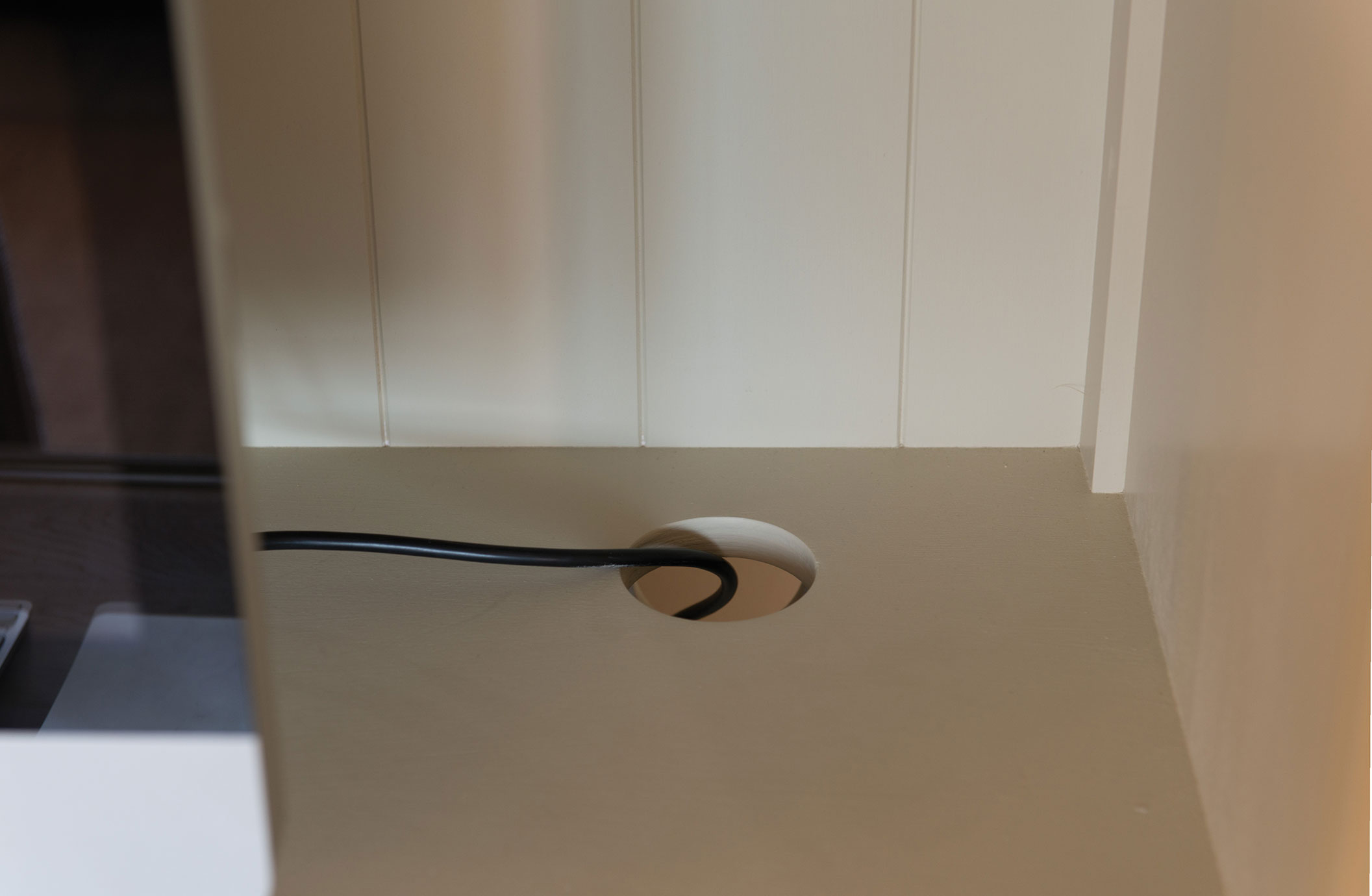 Nahaufnahme einer Kabeldurchführung in einer Schreibtischplatte mit schwarzem Kabel, ideal für sauberes Kabelmanagement