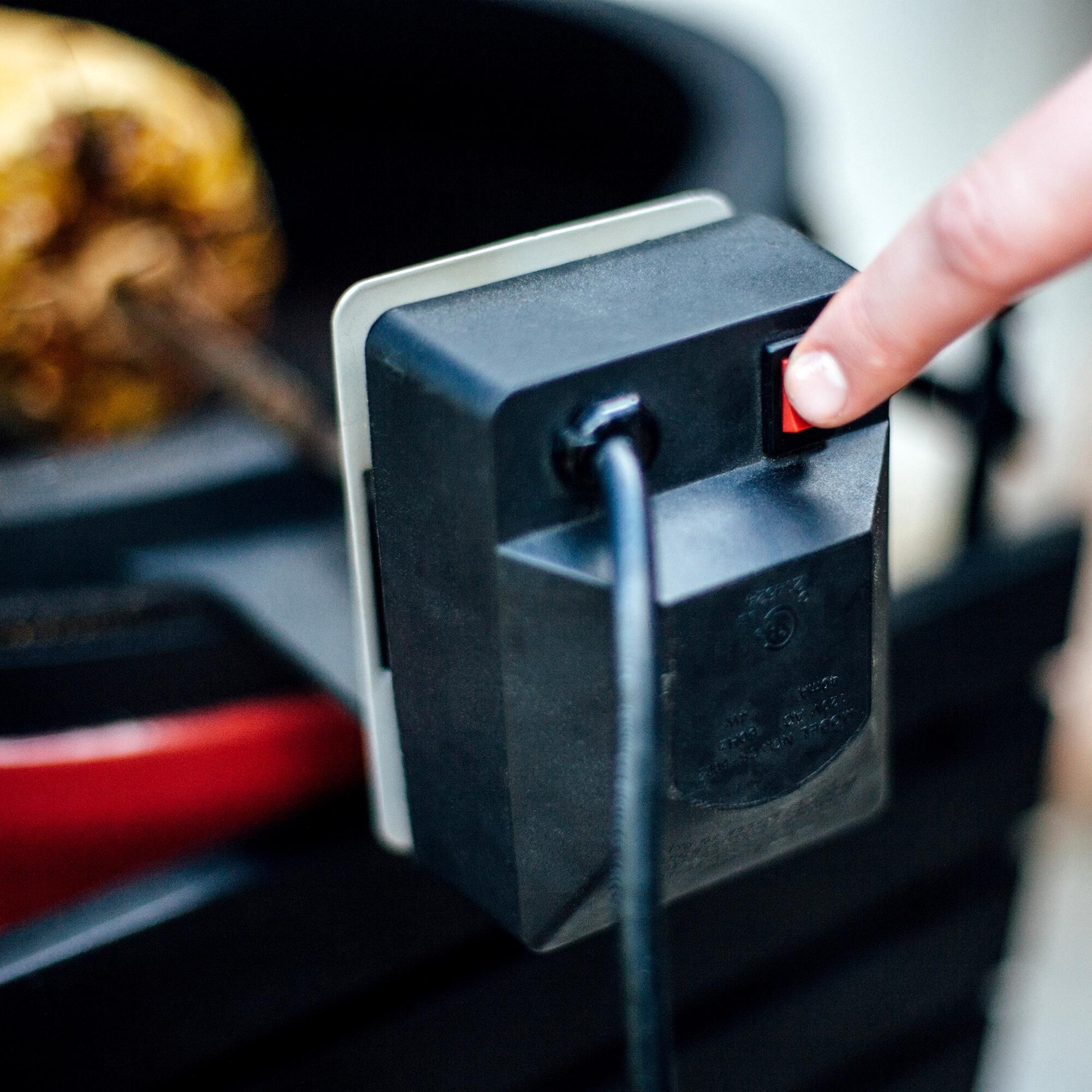 Nahaufnahme eines Fingers, der den roten An-/Ausschalter eines elektrischen Grillmotors an einem Grill betätigt