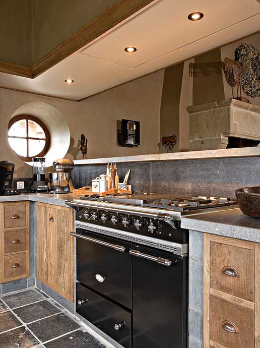 Gemütliche Landhausküche mit rustikalen Holzschränken, modernem Gasherd, Küchenmaschine, Kaffeemaschine und rundem Fenster