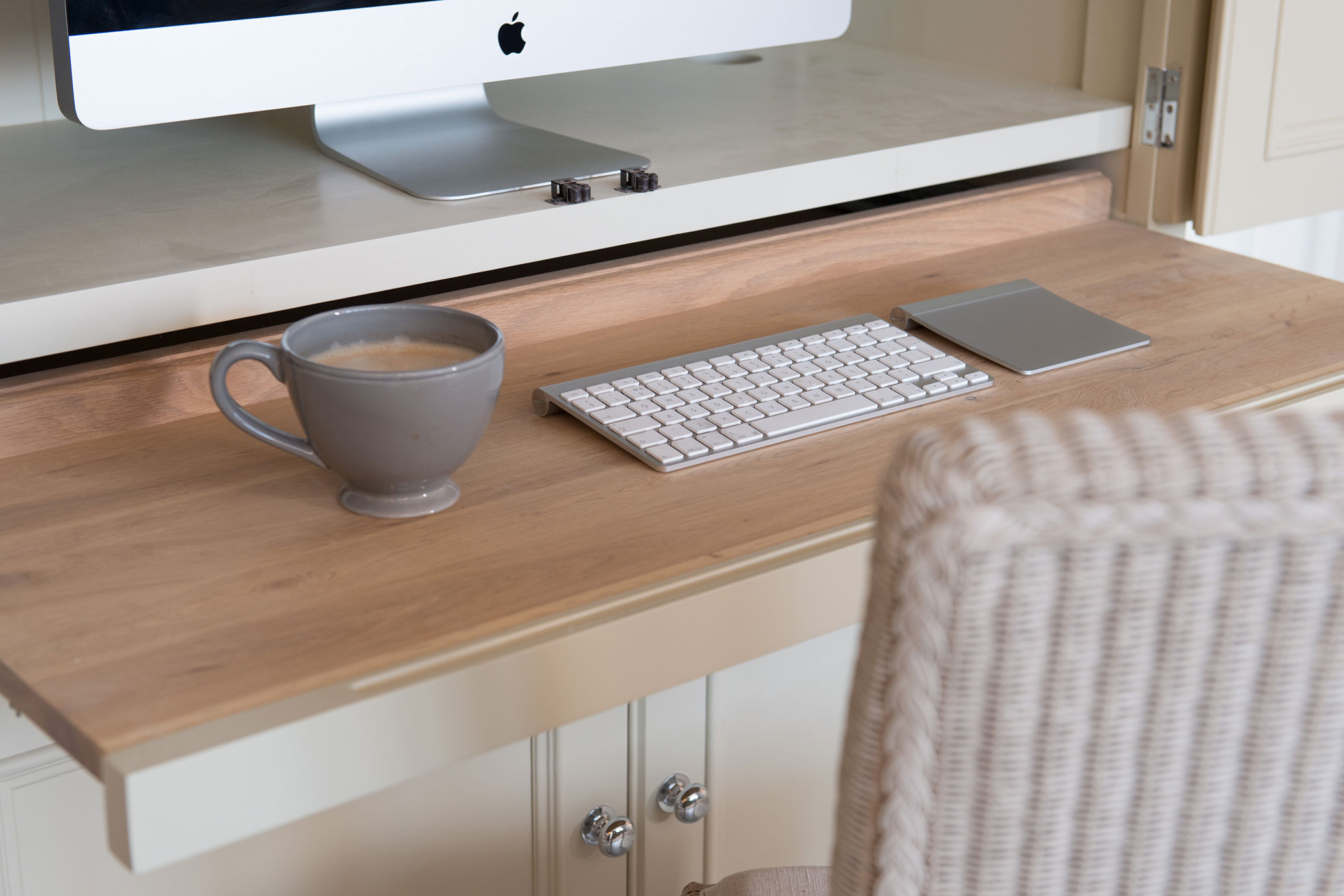 Arbeitsplatz mit iMac, weißer Tastatur, Touchpad und grauer Kaffeetasse auf einem hellen Holztisch in einem Home Office