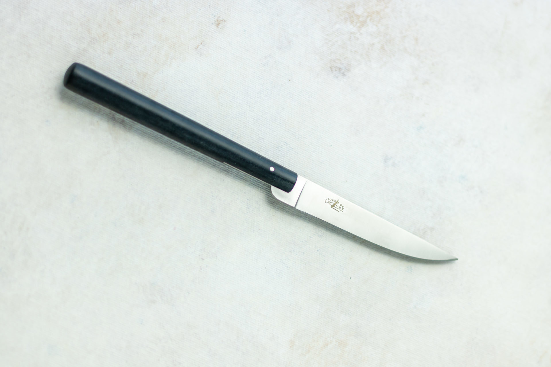 Abgebildet ist ein elegantes Laguiole Messer mit schwarzem, rundem Griff und glänzender Edelstahlklinge auf hellem Untergrund