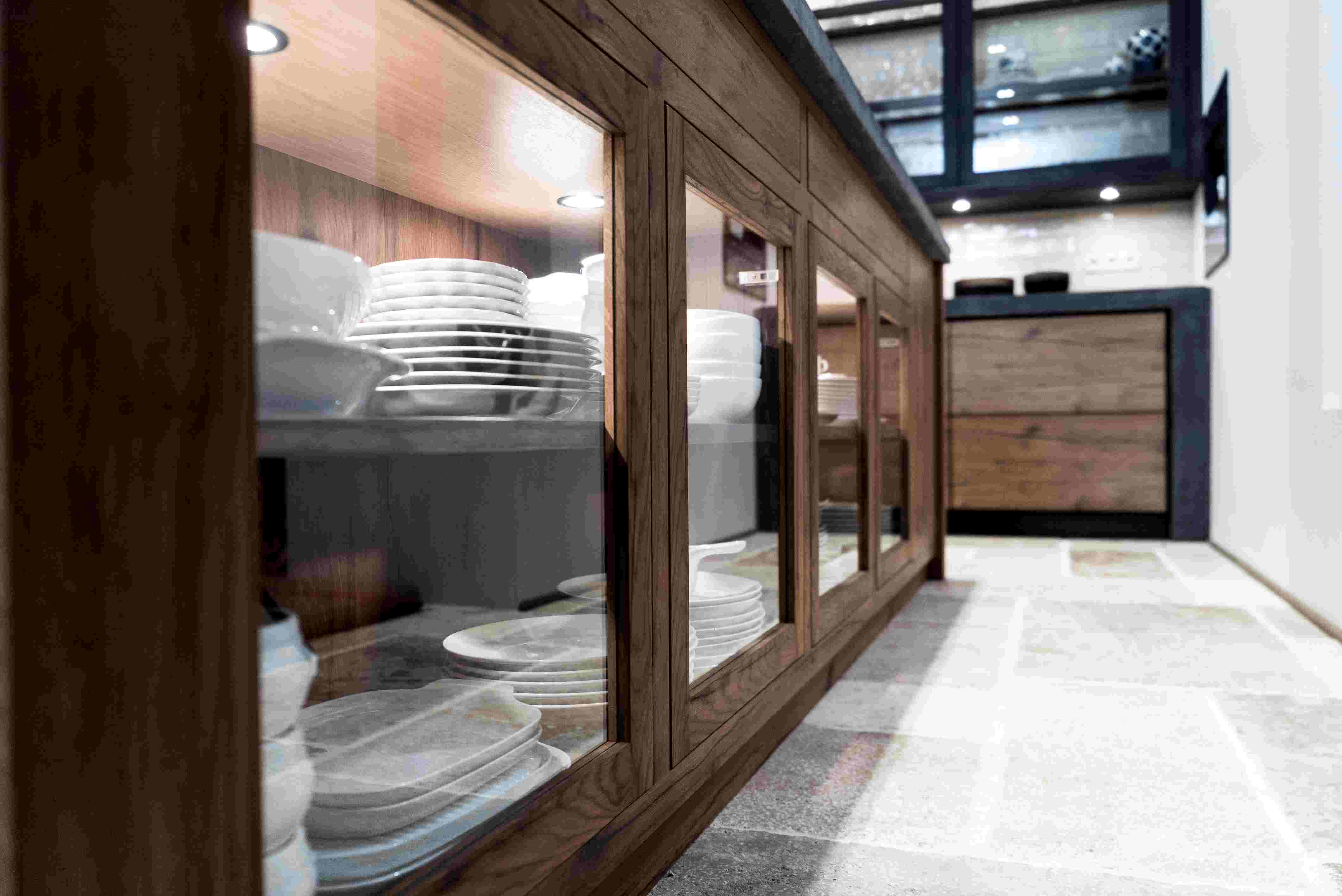 Nahaufnahme eines eleganten Küchenschranks aus Holz mit Glastüren, gefüllt mit gestapeltem weißen Geschirr in einer modernen Küche