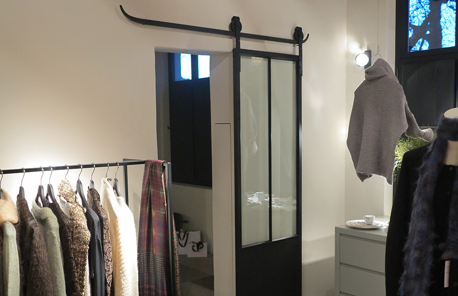 Modegeschäft mit Kleiderstange, verschiedenen Kleidungsstücken, einer modernen Schiebetür aus Glas und gemütlicher Einrichtung