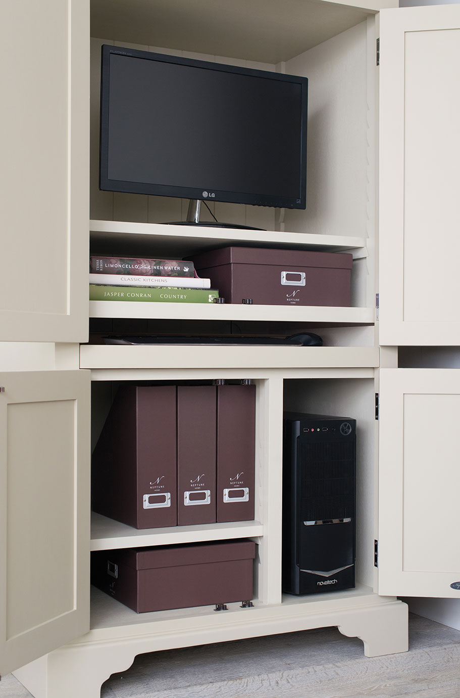 Geöffneter beiger Schrank mit Monitor, PC-Tower, braunen Aufbewahrungsboxen, Ordnern und Büchern, ideal für das Homeoffice