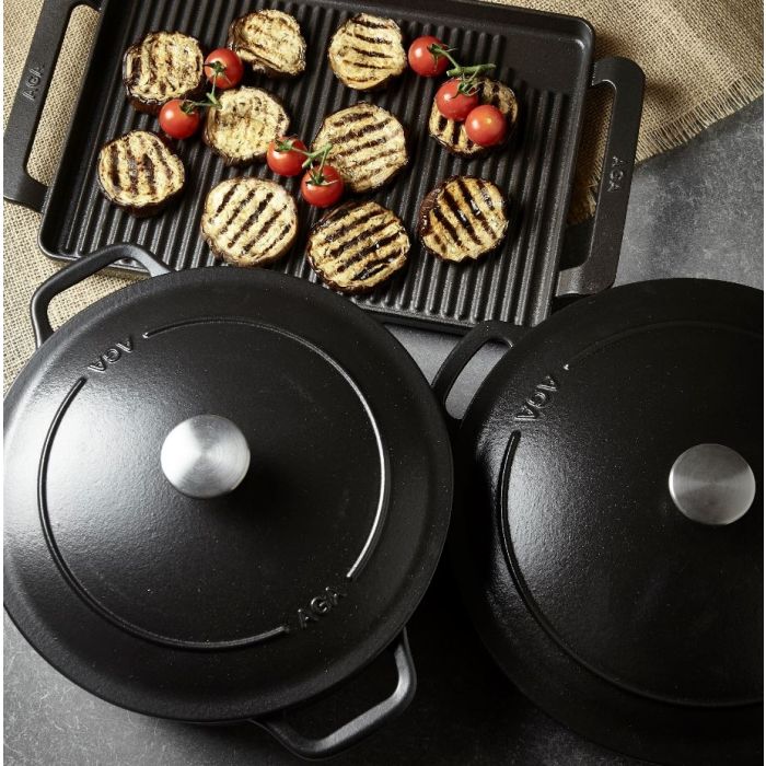 Zwei gusseiserne Kochtöpfe mit Deckel und eine Grillplatte mit gegrillten Auberginenscheiben und Kirschtomaten auf einem Küchentisch