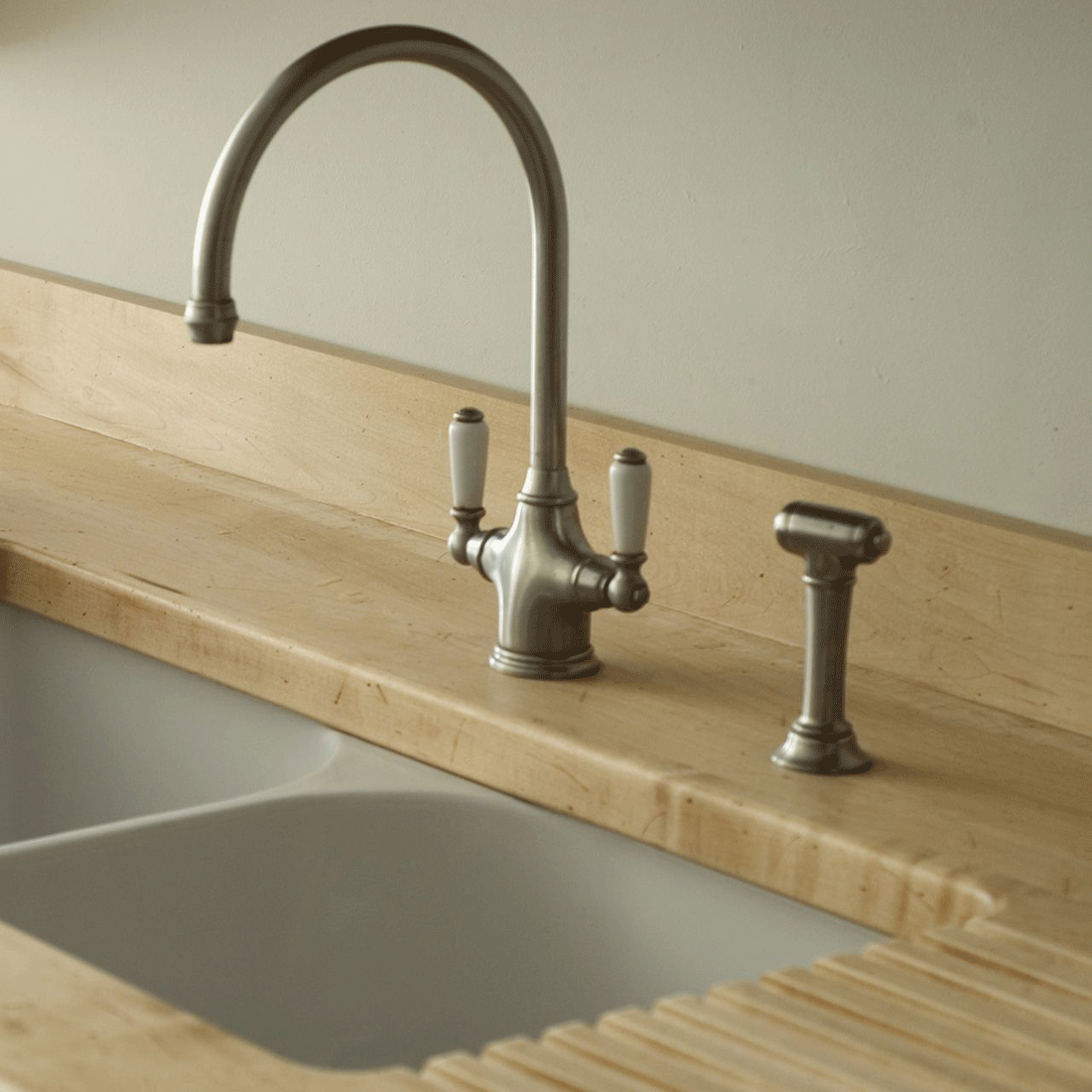 Elegante Küchenarmatur im Retro-Stil aus Edelstahl mit weißen Griffen, installiert auf einer Holzarbeitsplatte neben einem Waschbecken
