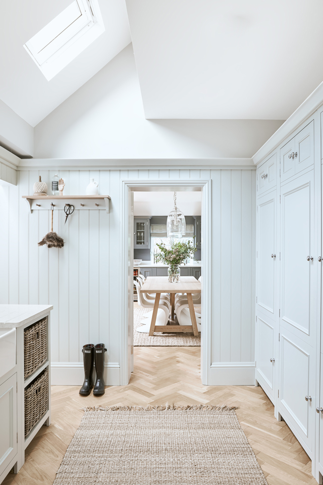 Lichtdurchfluteter Hausflur mit hellen Einbauschränken, geflochtenen Vorratskörben, schwarzen Gummistiefeln und dekorativem Blick in ein Esszimmer mit großem Holztisch und Blumenstrauß
