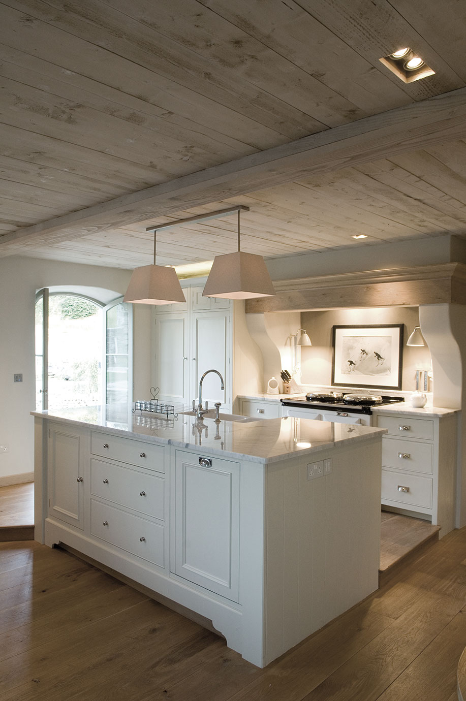 Helle Landhausküche mit Küchenschrank, Kochinsel mit Marmorarbeitsplatte, zwei Hängeleuchten und Holzfußboden