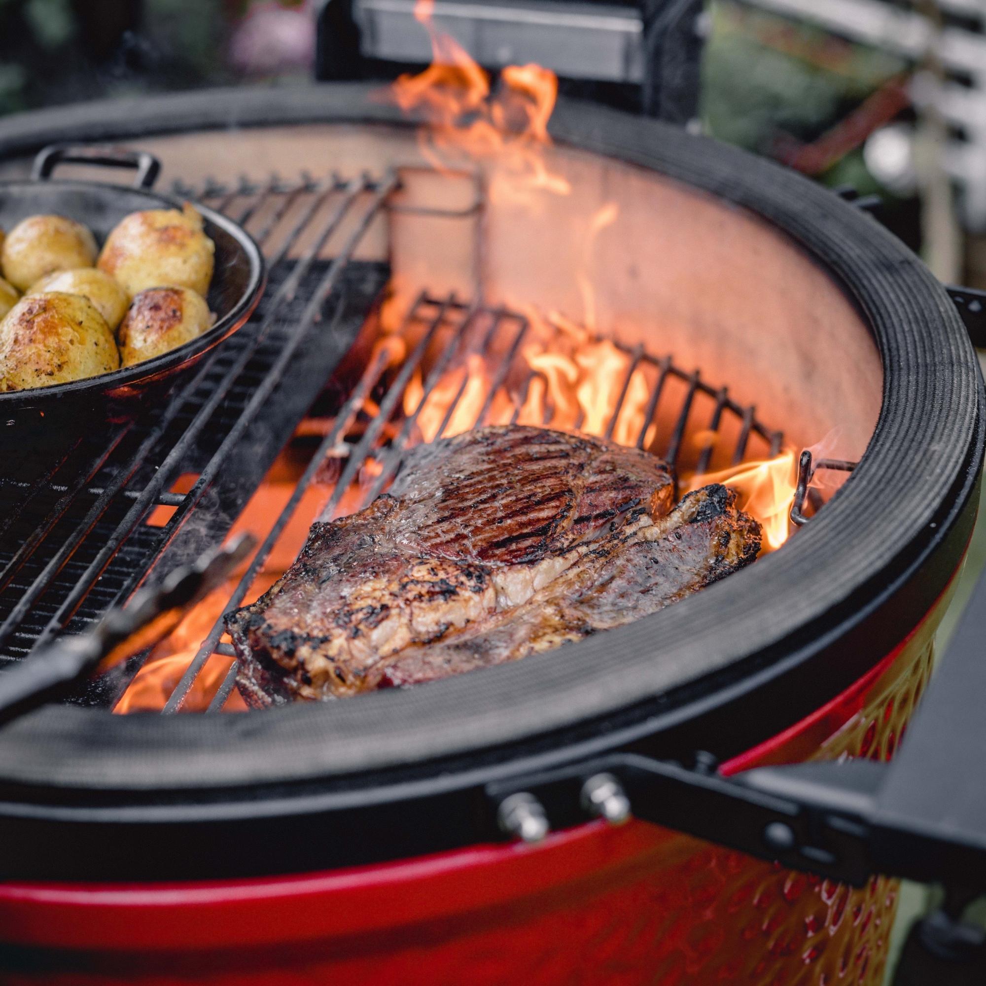 Steak und Kartoffeln werden auf einem modernen Keramikgrill mit großer Hitze und sichtbaren Flammen gegrillt