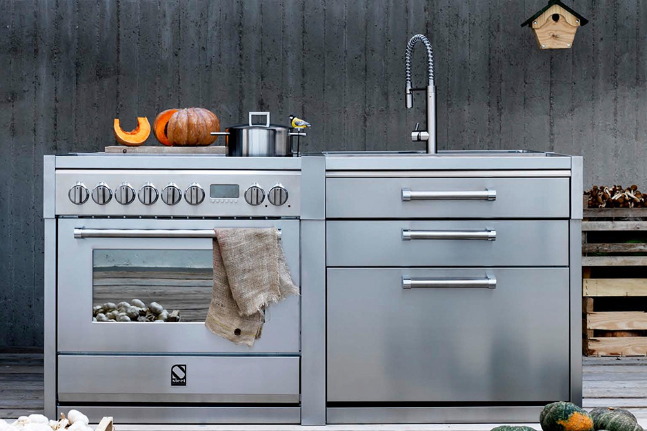 Edelstahl-Outdoor-Küche mit Herd, Backofen, Spülbecken und Arbeitsfläche, darauf Kürbis, Topf und Küchentuch