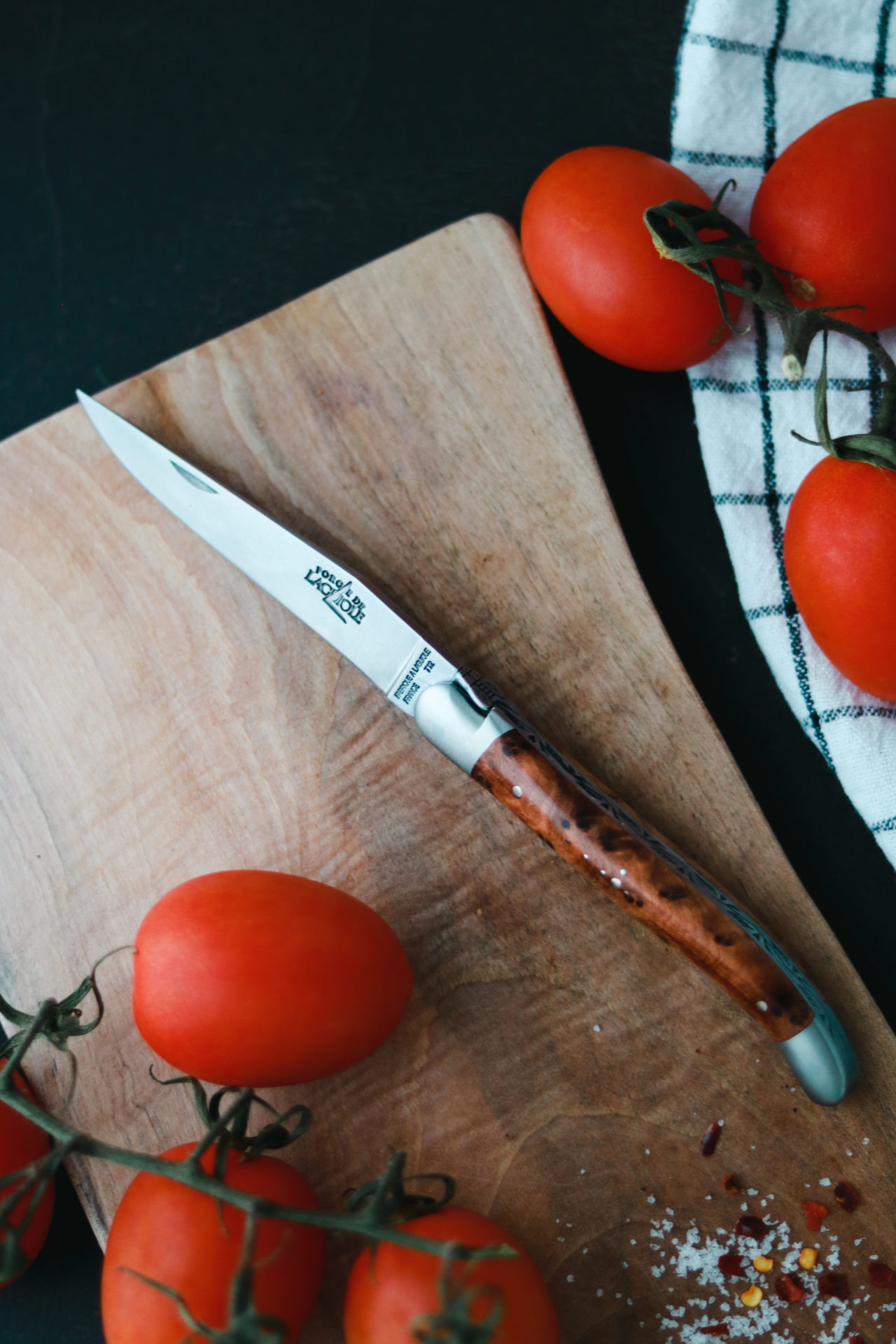 Küchenmesser mit elegantem Holzgriff liegt auf einem Holzbrett, umgeben von frischen Tomaten und Gewürzen