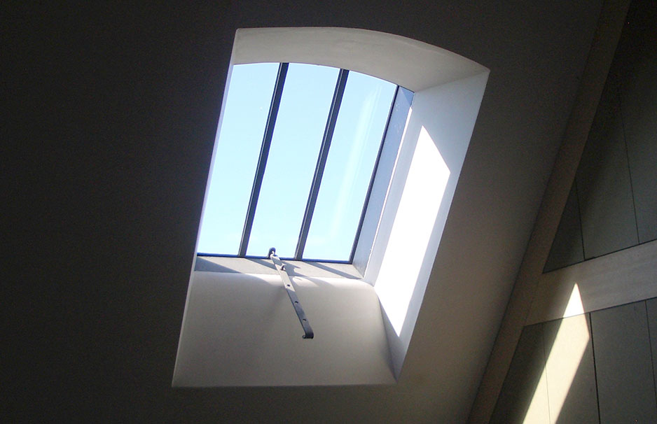 Großes Dachfenster mit blauen Glasflächen und Metallrahmen, das Sonnenlicht in einen modernen Innenraum lässt
