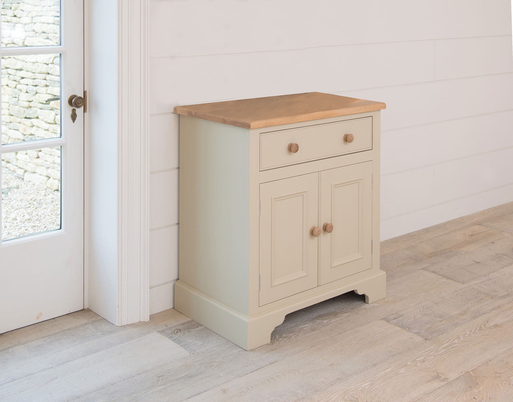Kommode im Landhausstil aus Holz, cremefarben lackiert, mit einer Schublade, zwei Türen und naturbelassener Holzoberfläche, in heller Raumumgebung
