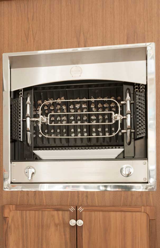 Modern eingebauter Gasgrill aus Edelstahl mit Drehspieß, eingebettet in einen Holzschrank