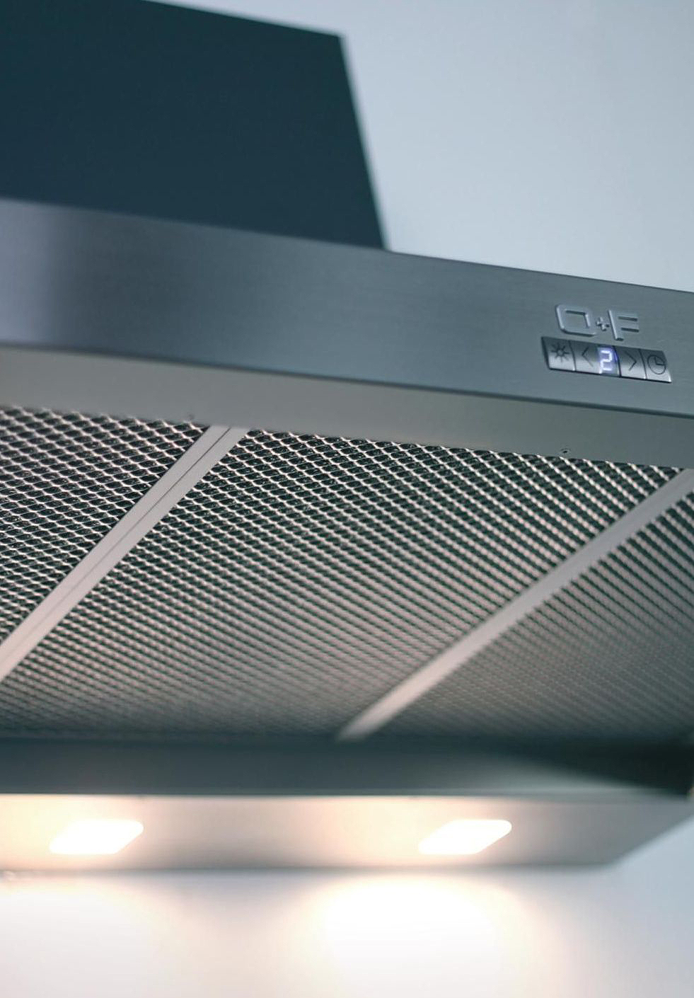 Detailansicht einer Edelstahl-Dunstabzugshaube mit sichtbarem Metallfilter, LED-Beleuchtung und elektronischem Bedienfeld