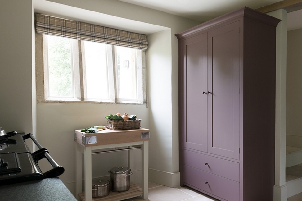 Küche mit fliederfarbenem Schrank, Fenster mit Rollos und kleinem Küchenwagen mit Gemüsekorb