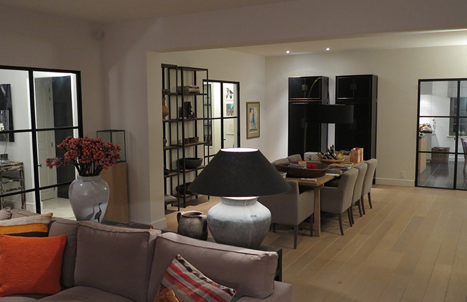 Gemütliches Wohnzimmer mit Sofa, farbigen Kissen, großem Lampenschirm, Essbereich, dekorativer Vase mit roten Blumen und modernen Regalen
