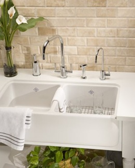 Weiße Doppelspüle mit verchromten Wasserhähnen, Handtuch, Gläsern und Vase vor beige Ziegelwand in moderner Küche