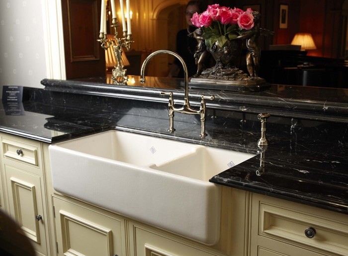 Weiße Keramikspüle in einer luxuriösen Küche mit schwarzer Marmorplatte, goldenen Armaturen und Blumendeko