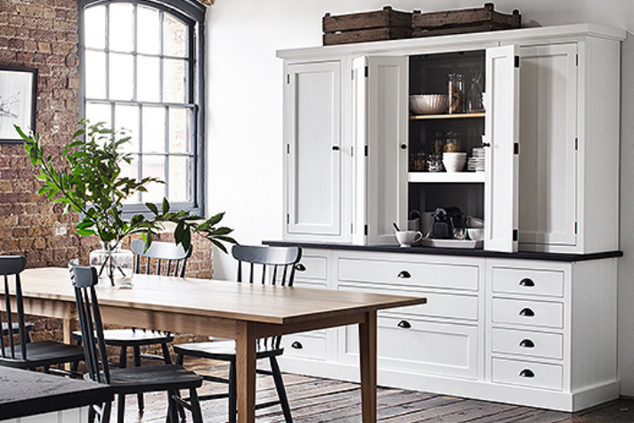 Helle Küche im Landhausstil mit großem weißen Schrank, Holztisch, schwarzen Stühlen und dekorativen Elementen