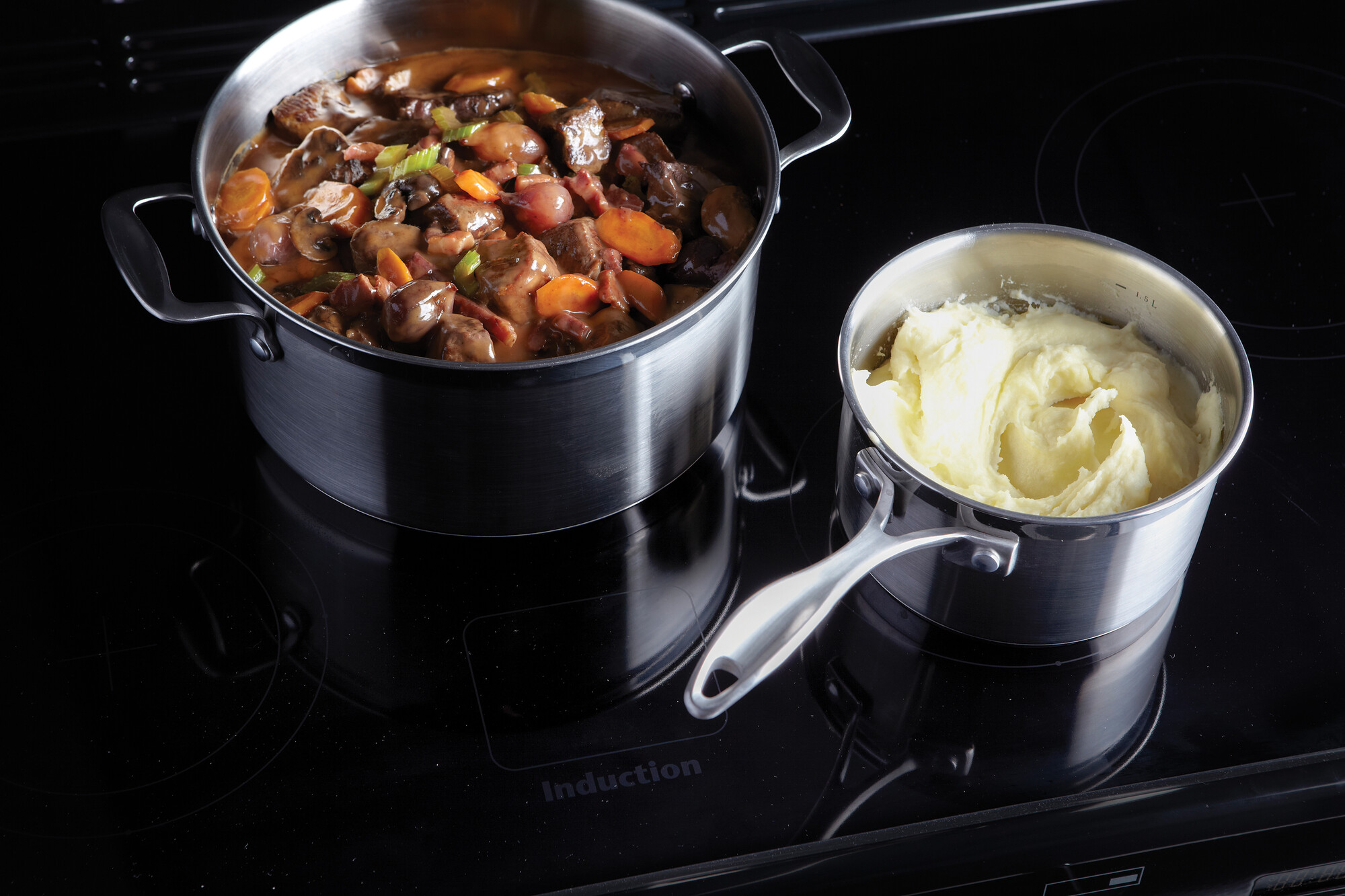 Zwei Töpfe auf einem Induktionsherd, einer gefüllt mit Rindergulasch und Gemüse, der andere mit frischem Kartoffelpüree