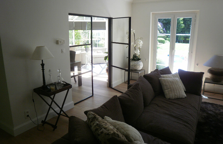 Gemütliches Wohnzimmer mit braunem Sofa, Glastür und Blick auf den Garten durch große Terrassentüren.
