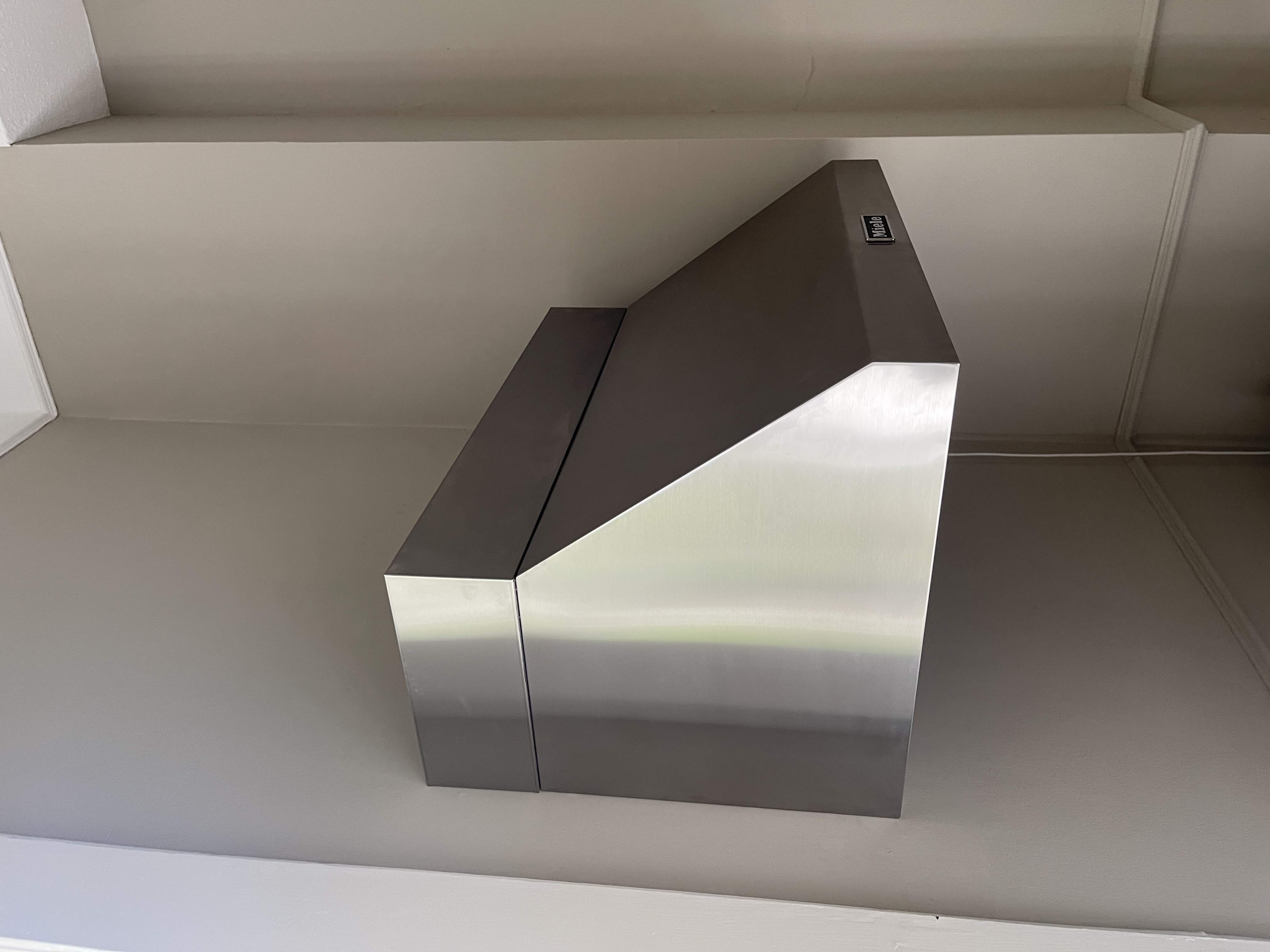 Edelstahl-Dunstabzugshaube von Miele in einer modernen Küche an einer hellen Wand montiert