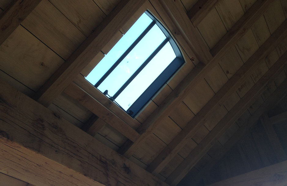 Blick von innen auf ein geöffnetes Dachfenster mit Holzrahmen in einer Holzbalkendecke
