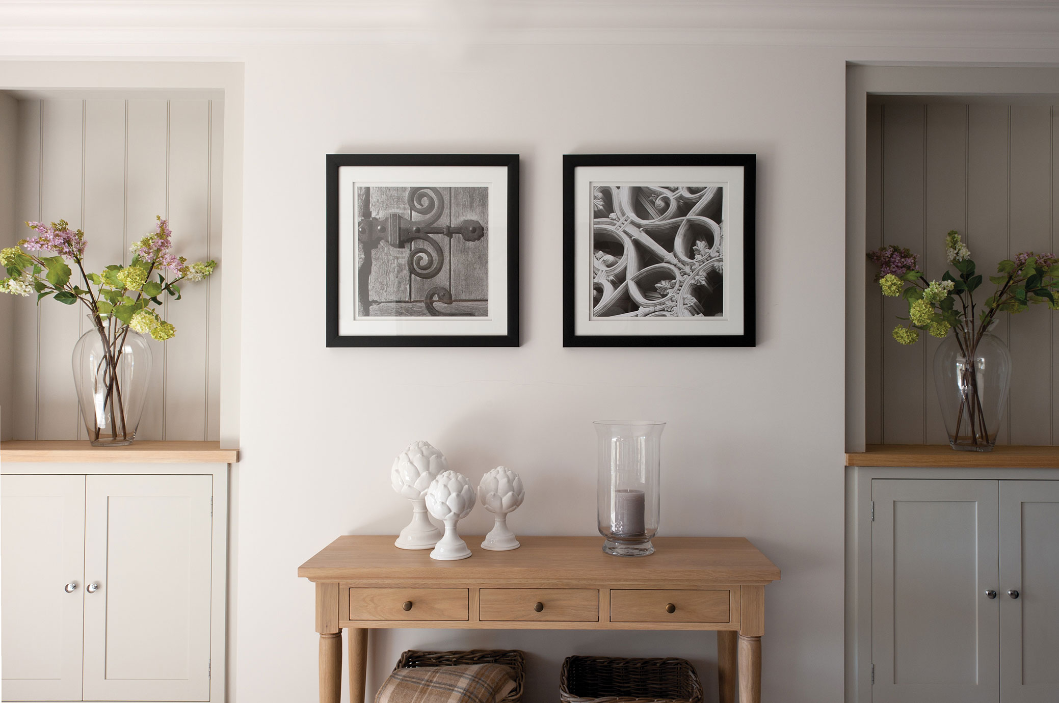 Heller Eingangsbereich mit Holztisch, dekorativen weißen Figuren, Windlicht und Glasvasen mit Blumen, dazu zwei Schwarzweiß-Bilder an der Wand