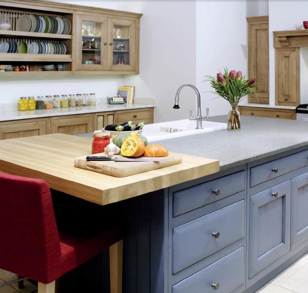 Große Küche im Landhausstil mit blaugrauen Unterschränken, Holzelementen, Kücheninsel, Spüle, Blumenstrauß und Gemüse auf dem Schneidebrett