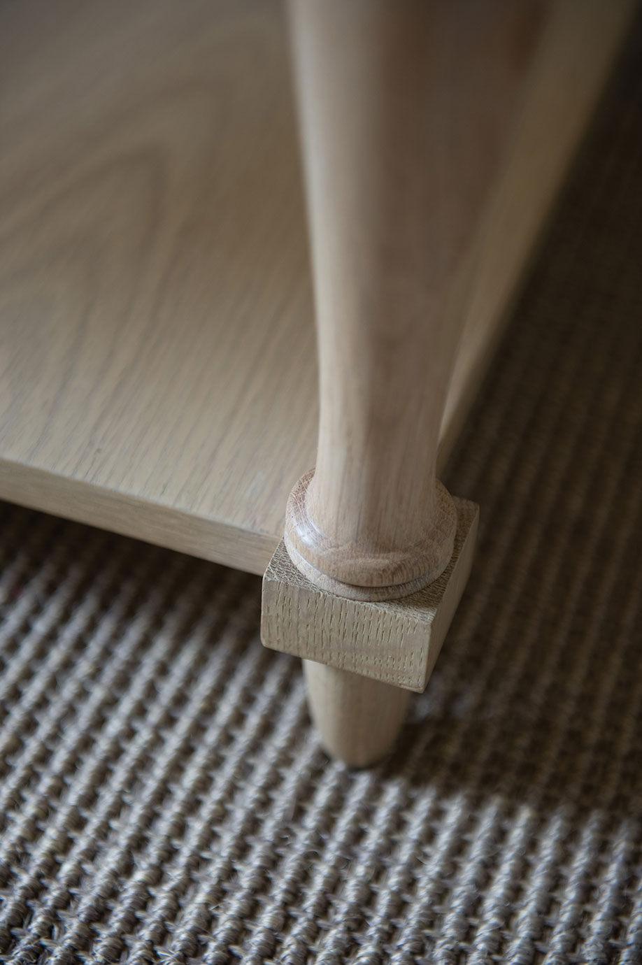 Nahaufnahme eines Tischbeins aus Holz, das an einem Möbelstück befestigt ist, auf einem strukturierten Teppichboden