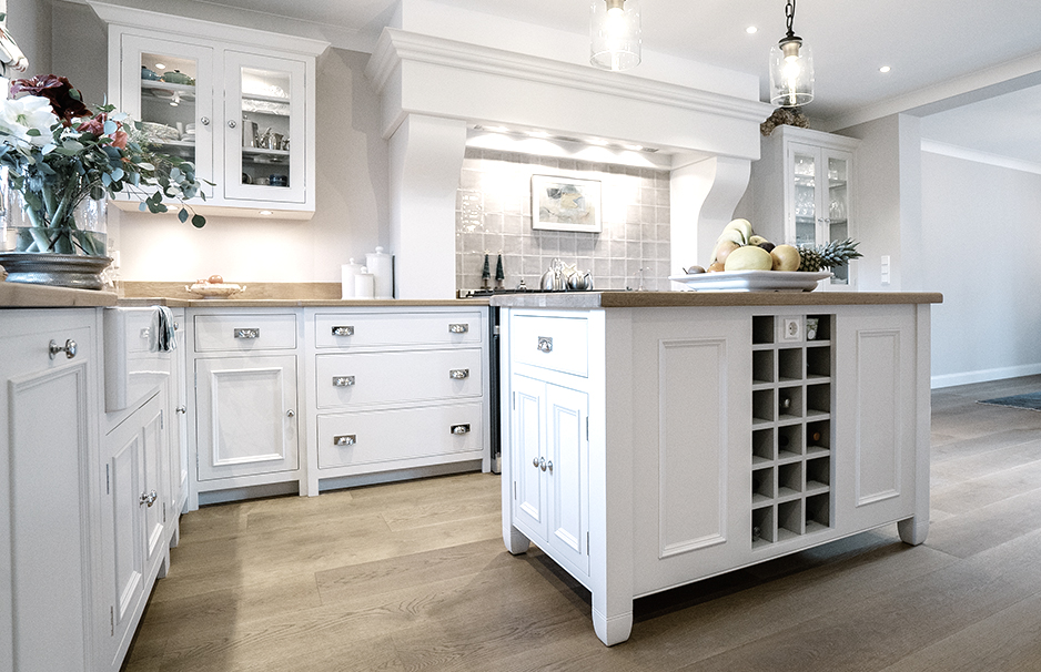 Helle, moderne Landhausküche mit weißer Kochinsel, integriertem Weinregal, Obstschale und großzügigem Stauraum auf hellem Holzboden