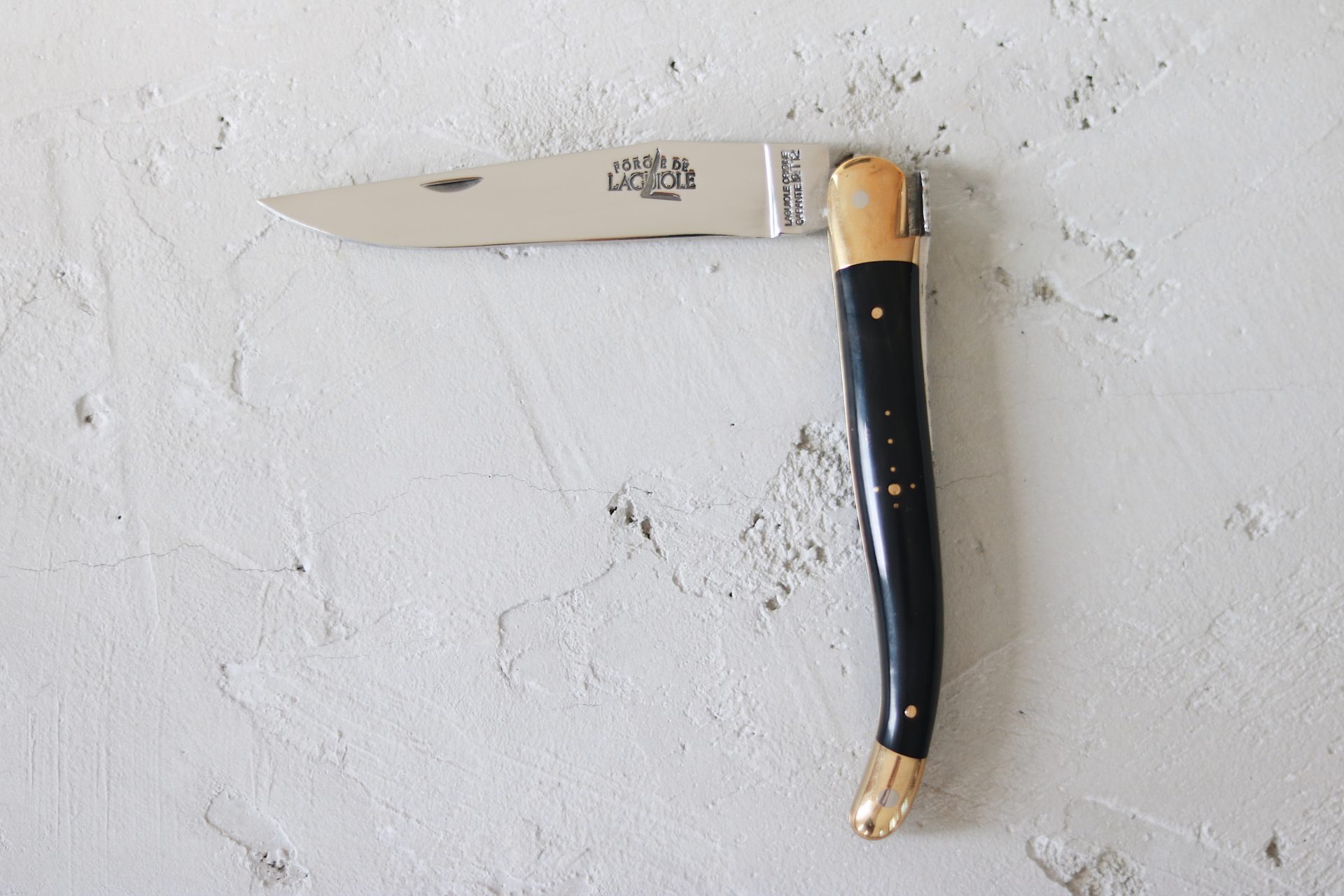 Elegantes Laguiole Taschenmesser mit schwarz-goldenem Griff und eingeklapptem Edelstahl-Messer auf hellem Untergrund