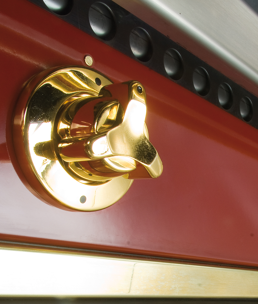 Goldener Drehgriff aus Metall an einem roten Küchengerät oder Ofen