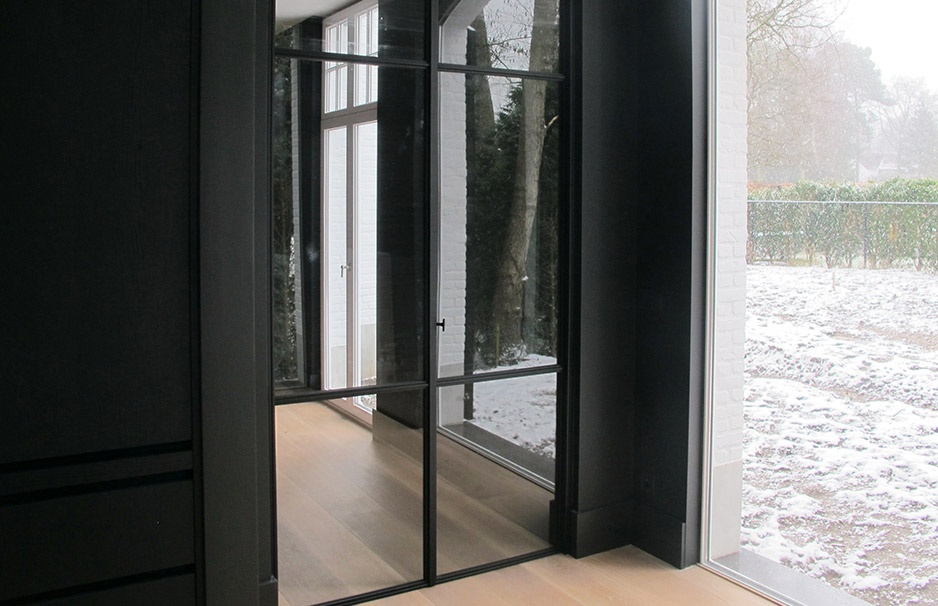 Schwarze Stahl-Glas-Tür in einem modernen Wohnraum, dahinter ist ein Schneegarten durch große Fenster zu sehen