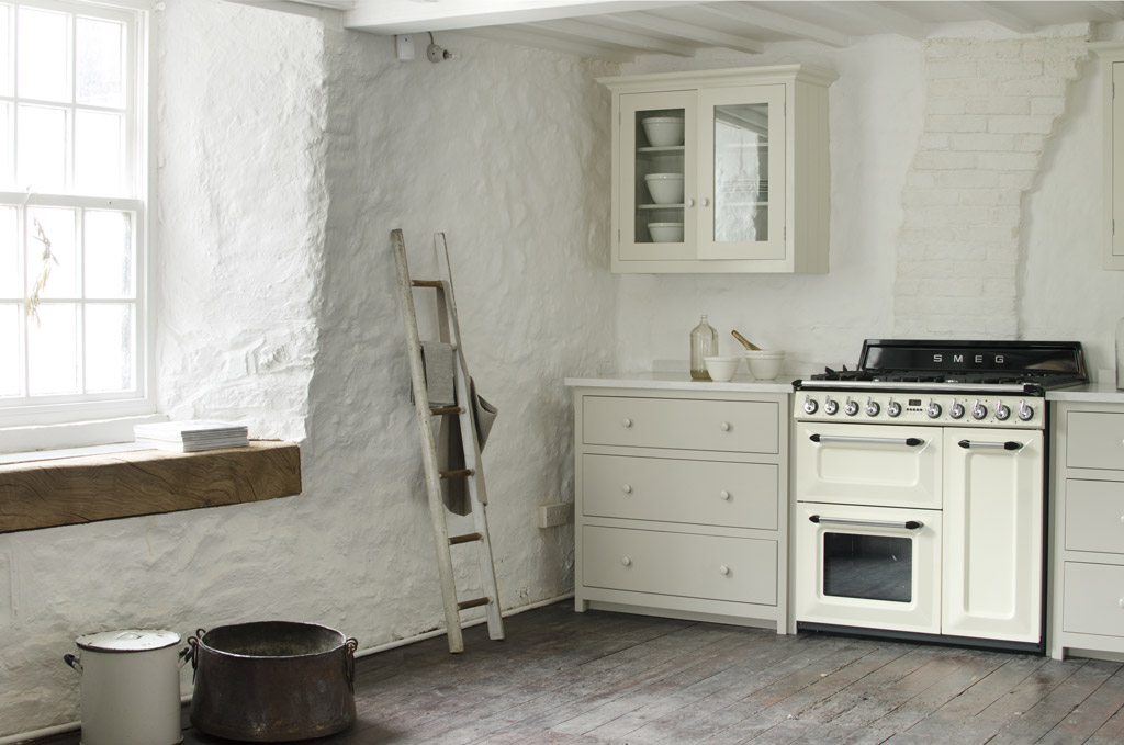 Gemütliche Küche im Landhausstil mit cremefarbenem SMEG Herd, weißen Schränken, Holzleiter und rustikalem Holzboden
