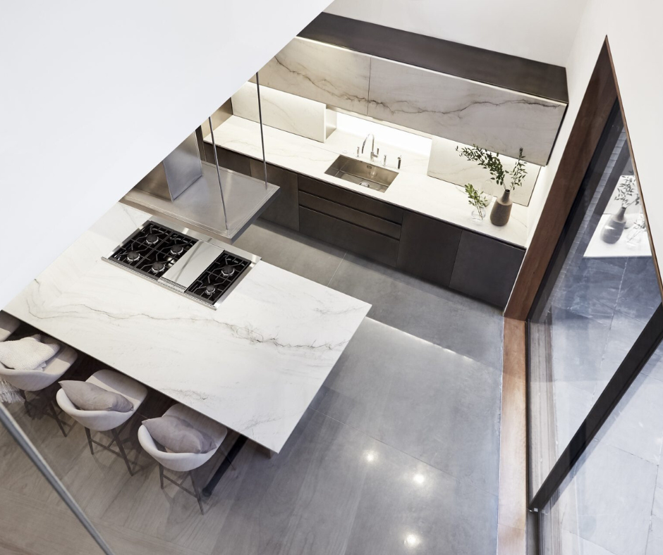 Helle, moderne Küche mit großer Marmor-Arbeitsplatte, Gasherd, Barhockern sowie eleganten, dunklen Unterschränken und minimalistischer Dekoration
