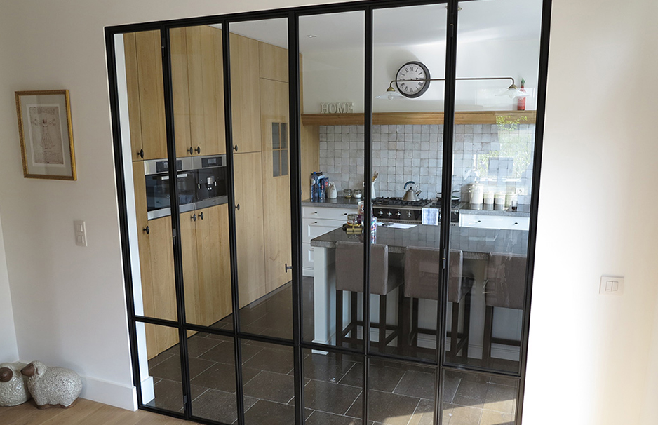 Raumtrenner aus schwarzem Metall und Glas trennt offene Küche mit Holzschränken und Kücheninsel vom Wohnbereich ab