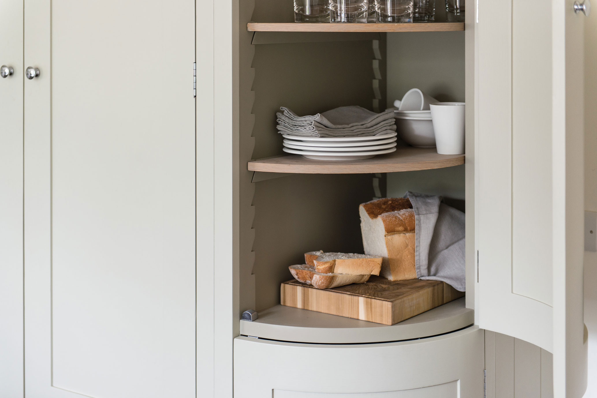 Eckeinbauschrank in einer modernen Küche mit Gläsern, Tellern, Servietten und frisch angeschnittenem Brot auf einem Holzbrett
