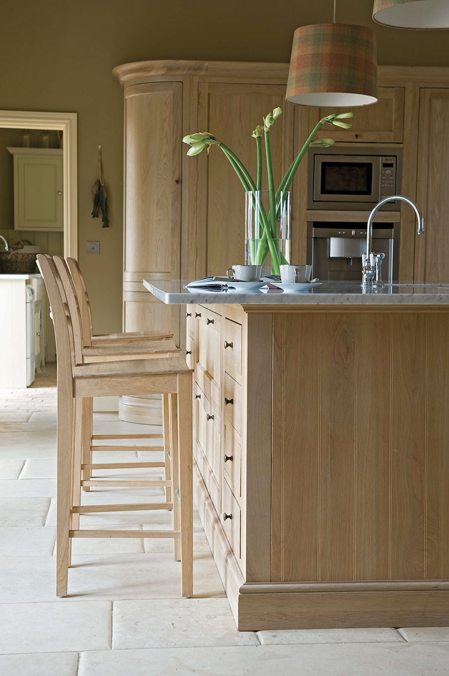 Kücheninsel aus hellem Holz mit zwei Hochstühlen, Vase mit Blumen, Spüle und Kaffeeservice in einer modernen Küche