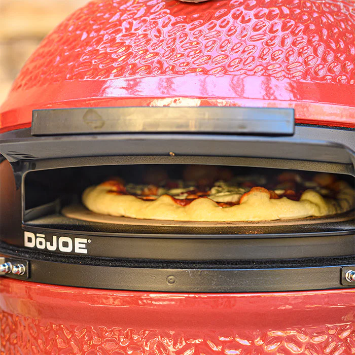 Frisch belegte Pizza wird im DoJoe Pizzaaufsatz auf einem roten Keramikgrill gebacken
